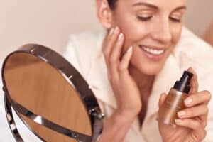 A woman applies Dead Sea skincare serum for rejuvenation, highlighting facial beauty and skincare benefits, with a mirror reflecting her face.