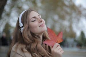 Autumn woman enjoying nature with leaf, skincare, relaxation, natural beauty, outdoor, serene face, wellness, peaceful, mindfulness, healthy skin, Dead Sea cosmetics, self-care.