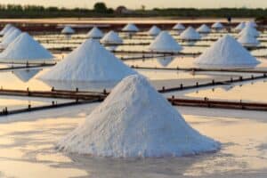 Salt harvesting in the Dead Sea with white salt mounds reflected in water.