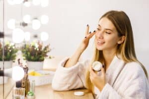 Silky moisturizer application by a young woman in a cozy bathroom, featuring Dead Sea skincare products, promoting healthy skin with natural ingredients.